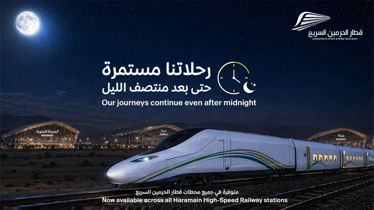 Night-time image of a white high-speed train on tracks with illuminated stations in the background; Arabic and English promo text about journeys continuing after midnight and availability across Haramain stations.